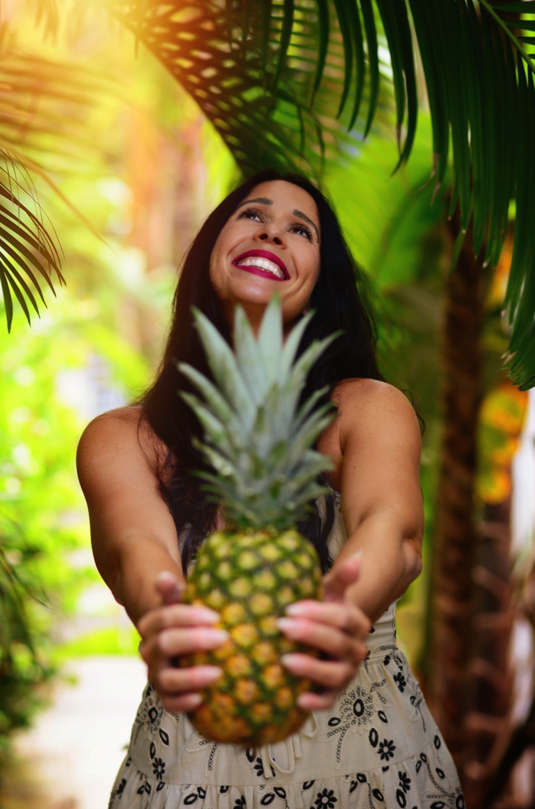 Jennifer Nicole offering a fresh pineapple beneath the palms