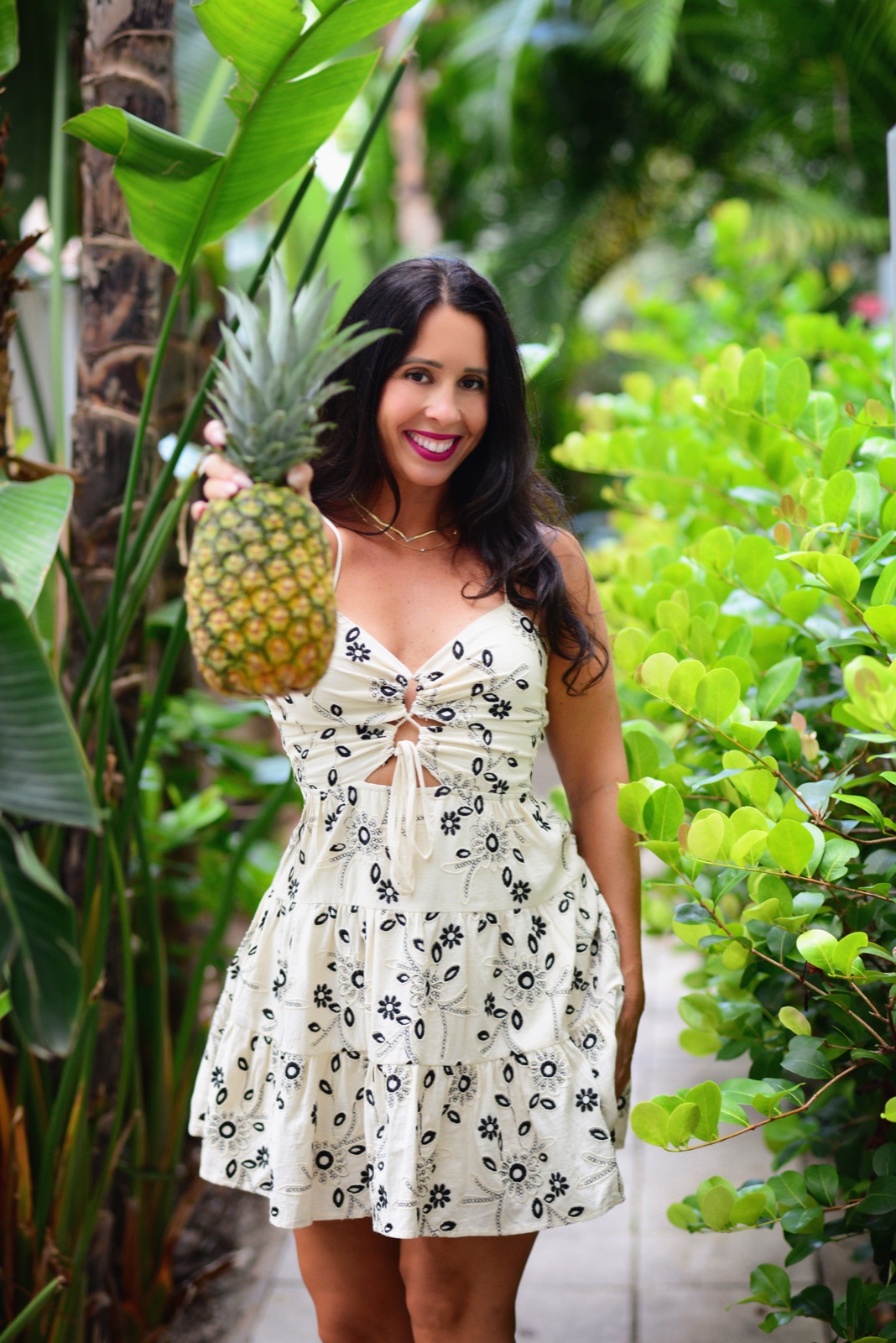 Jennifer Nicole offering a fresh pineapple on a tropical garden path