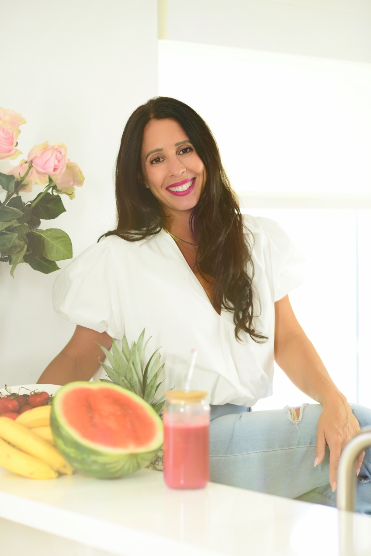 Jennifer Nicole seated at her kitchen counter with fresh fruit, roses and a pink smoothie